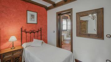 Een slaapkamer met een bed, een nachtkastje met lamp, een houten hoofdbord, een lijst met een foto aan de muur en een spiegel.