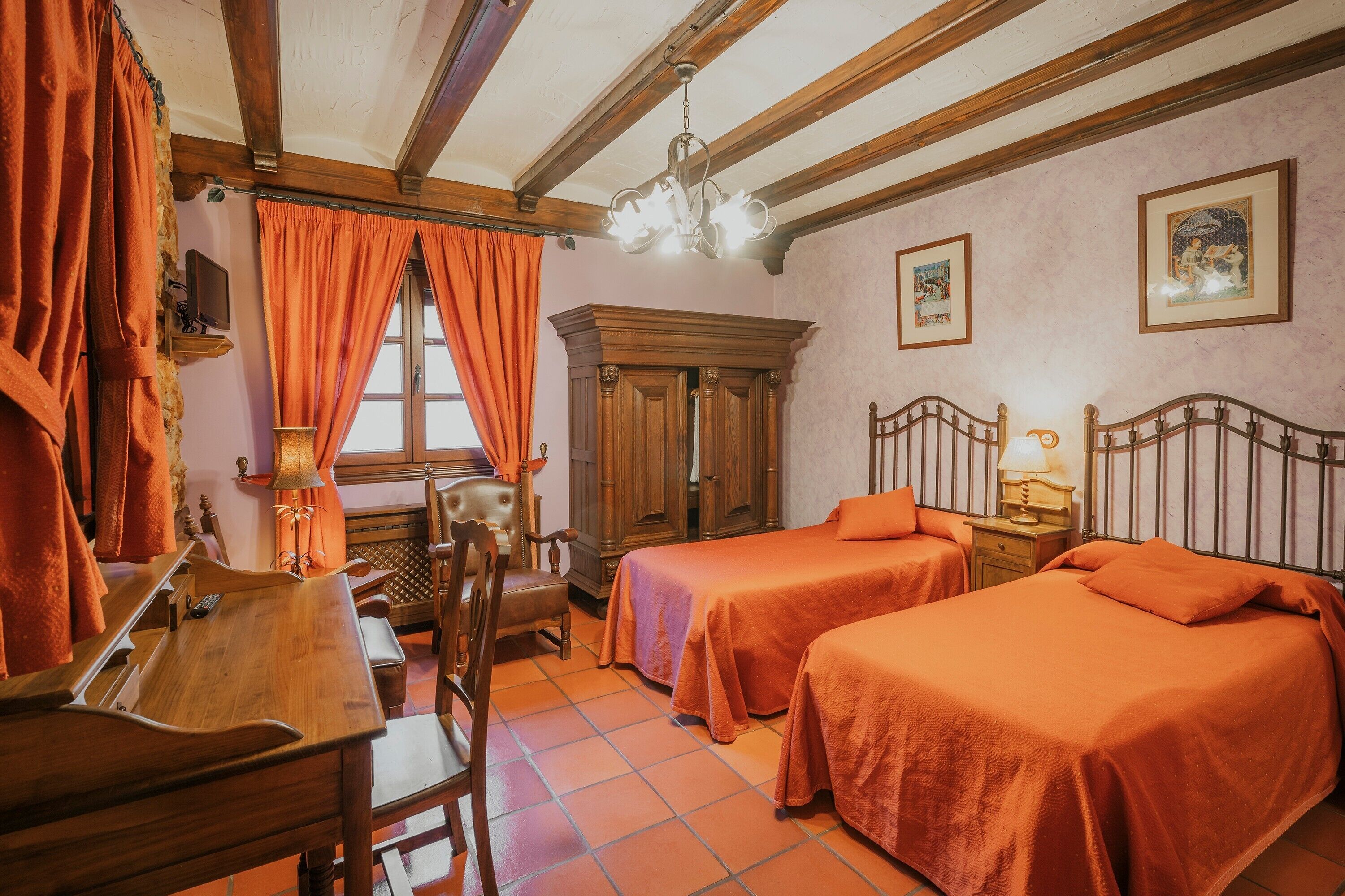 A room with two beds, a wooden desk, a chair, a cabinet, and a chandelier.