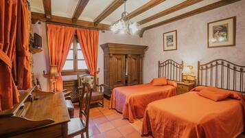 A room with two beds, a wooden desk, a chair, a cabinet, and a chandelier.
