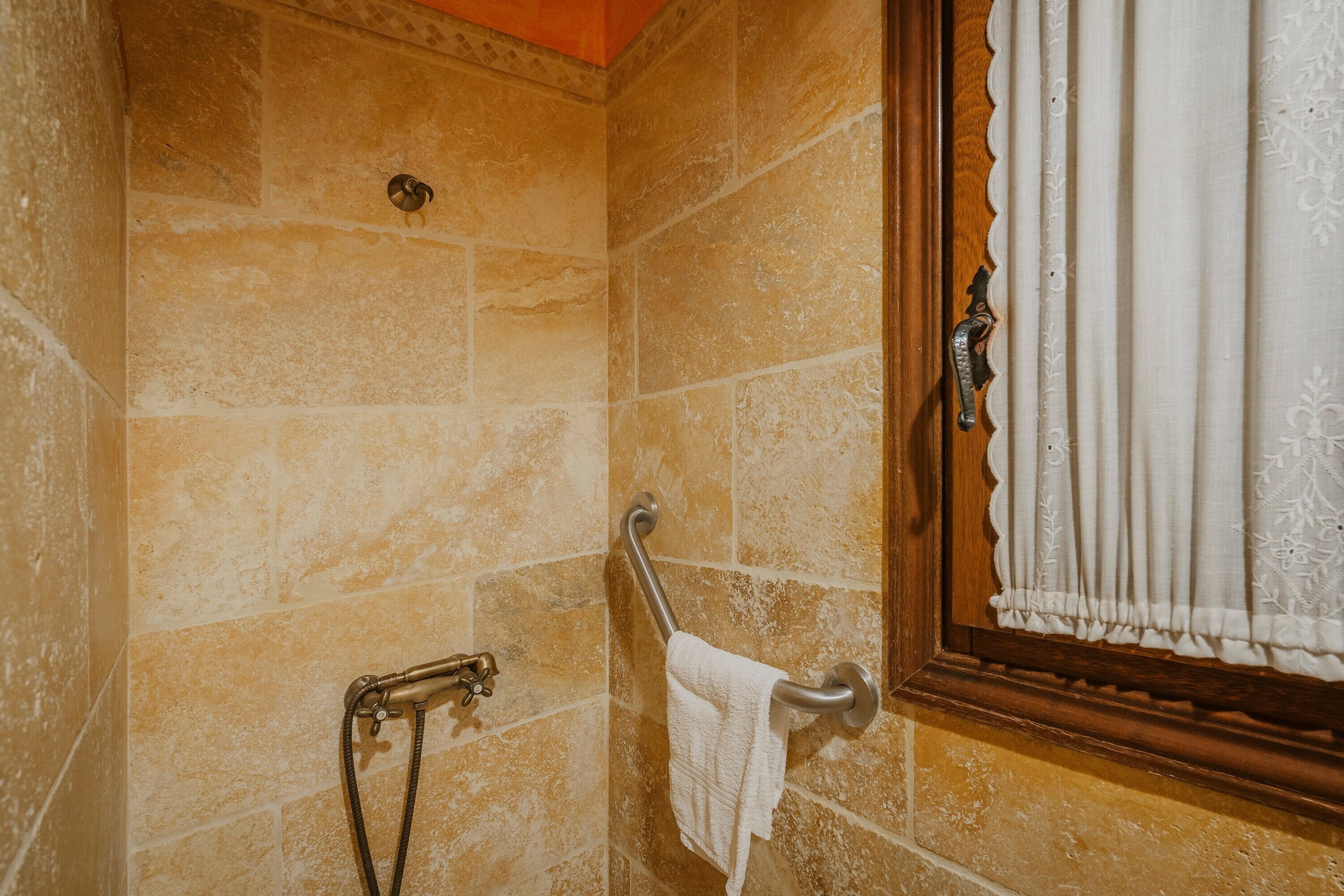 Une salle de bain avec des murs en pierre, une douche, un porte-serviettes et une fenêtre avec des rideaux.