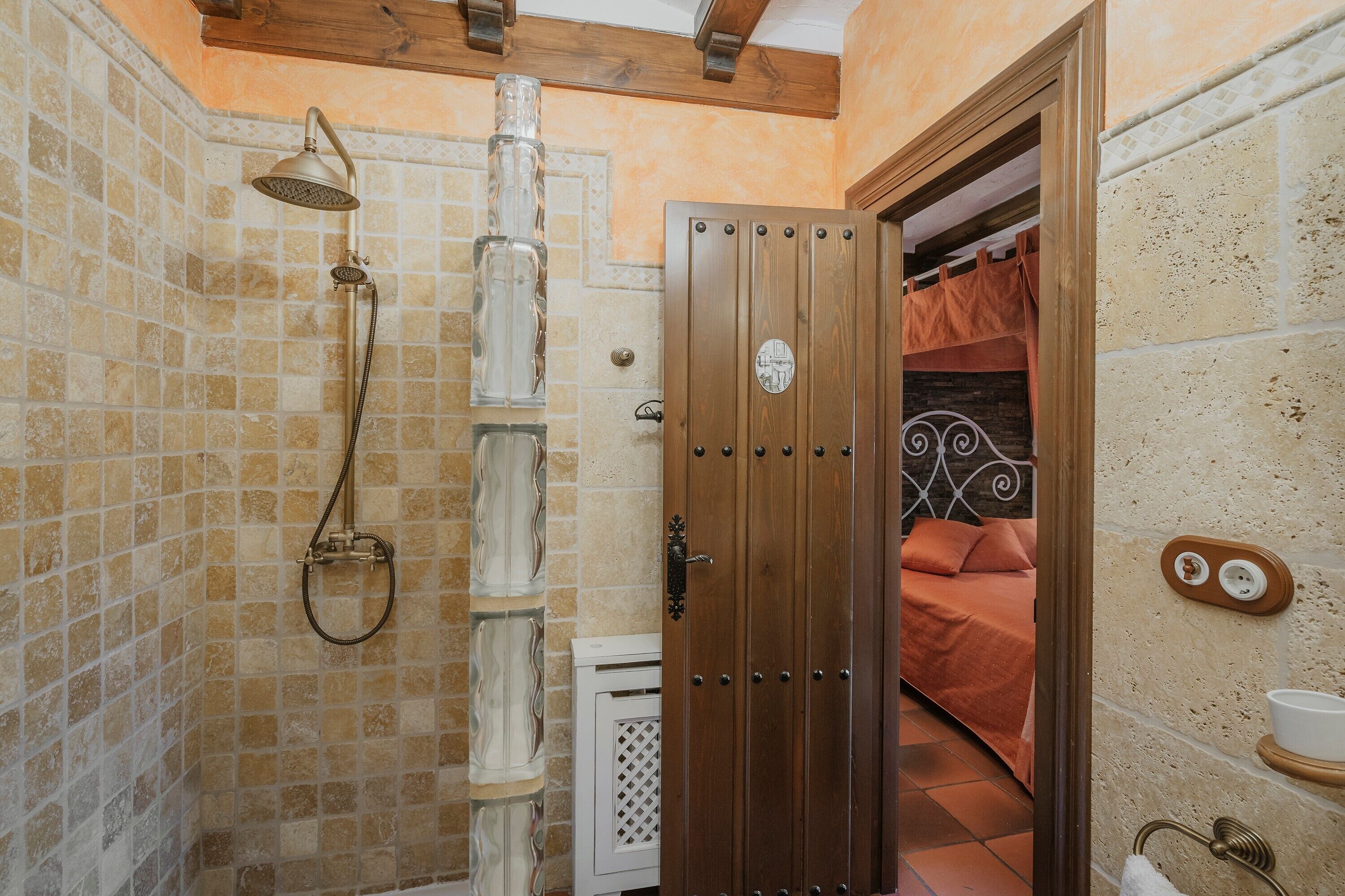 Un baño con ducha, una puerta de madera y una cama en la habitación contigua.