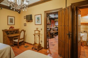 A room with a wooden desk, a chair, a small wooden stool, a television mounted on the wall, and a door leading to a bathroom. - Country House 'Los Beatos' with Shared Terrace, Private Garden and Wi-Fi (Urueña)