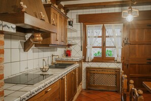Una cucina con mobili in legno, zoccolo paraschizzi rivestito di piastrelle, finestra con tende e lampadario.