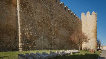 A stone wall with a tower, a grassy area with concrete benches, and a clear sky.