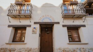 Um edifício com porta de madeira, duas varandas com grades de ferro forjado e uma placa acima da porta.