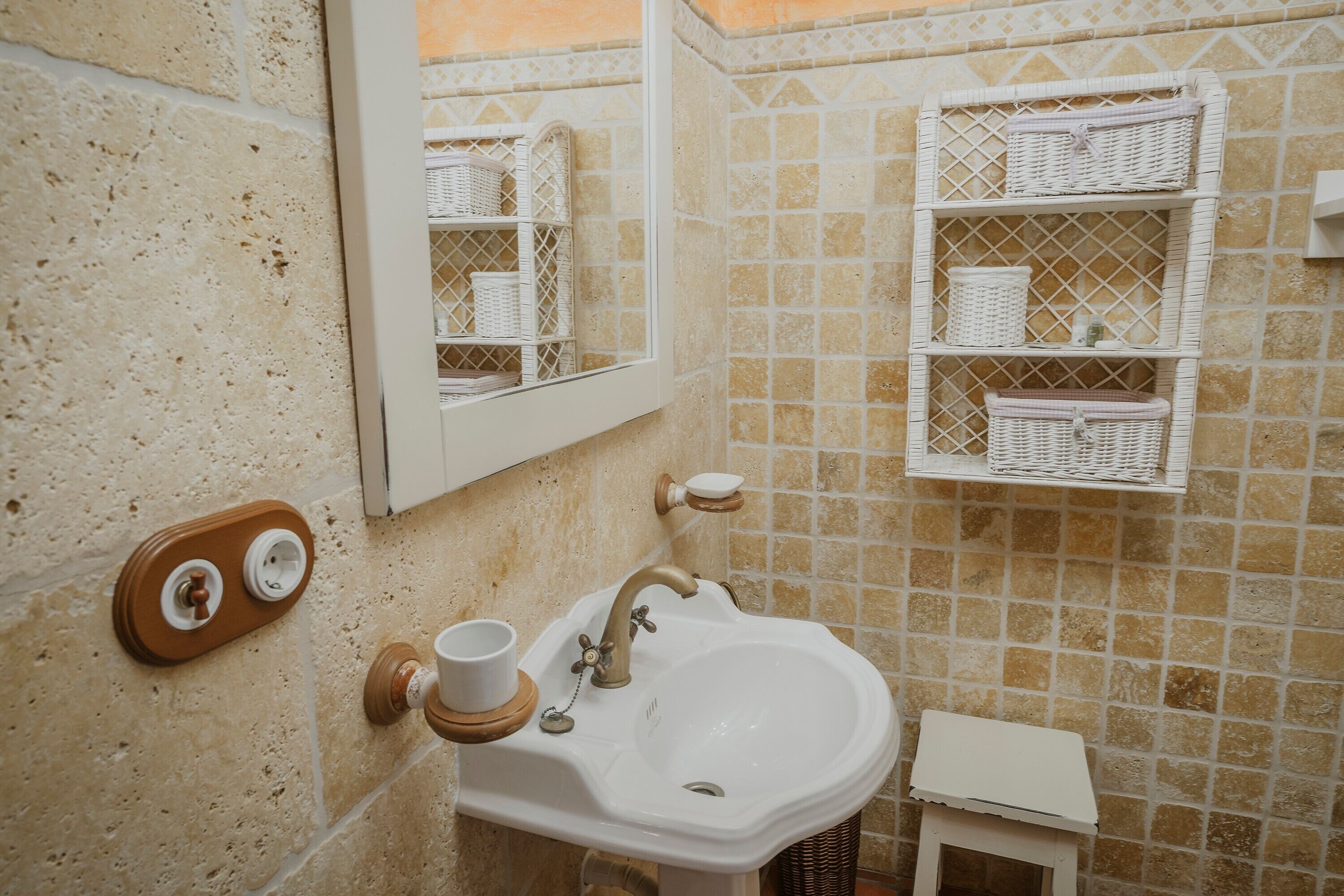 Une salle de bain avec un lavabo blanc, un miroir et des paniers en osier placés sur des étagères.