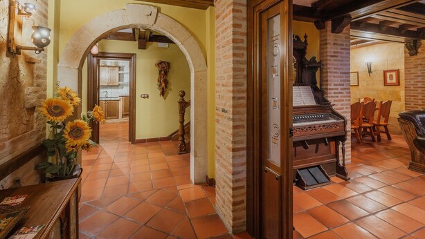 Um quarto espaçoso com um piano, uma área de refeições com cadeiras e uma cozinha visível através de um arco.