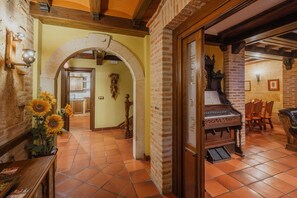 Un'ampia stanza con un pianoforte, un'area pranzo con sedie e una cucina visibile attraverso un arco.