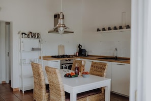 A compact kitchen with white cabinetry, a dining table with wicker chairs, a hanging light fixture, and a coffee machine. - Country House 'S'agret' with Mountain View, Private Pool and Wi-Fi (Capdepera)