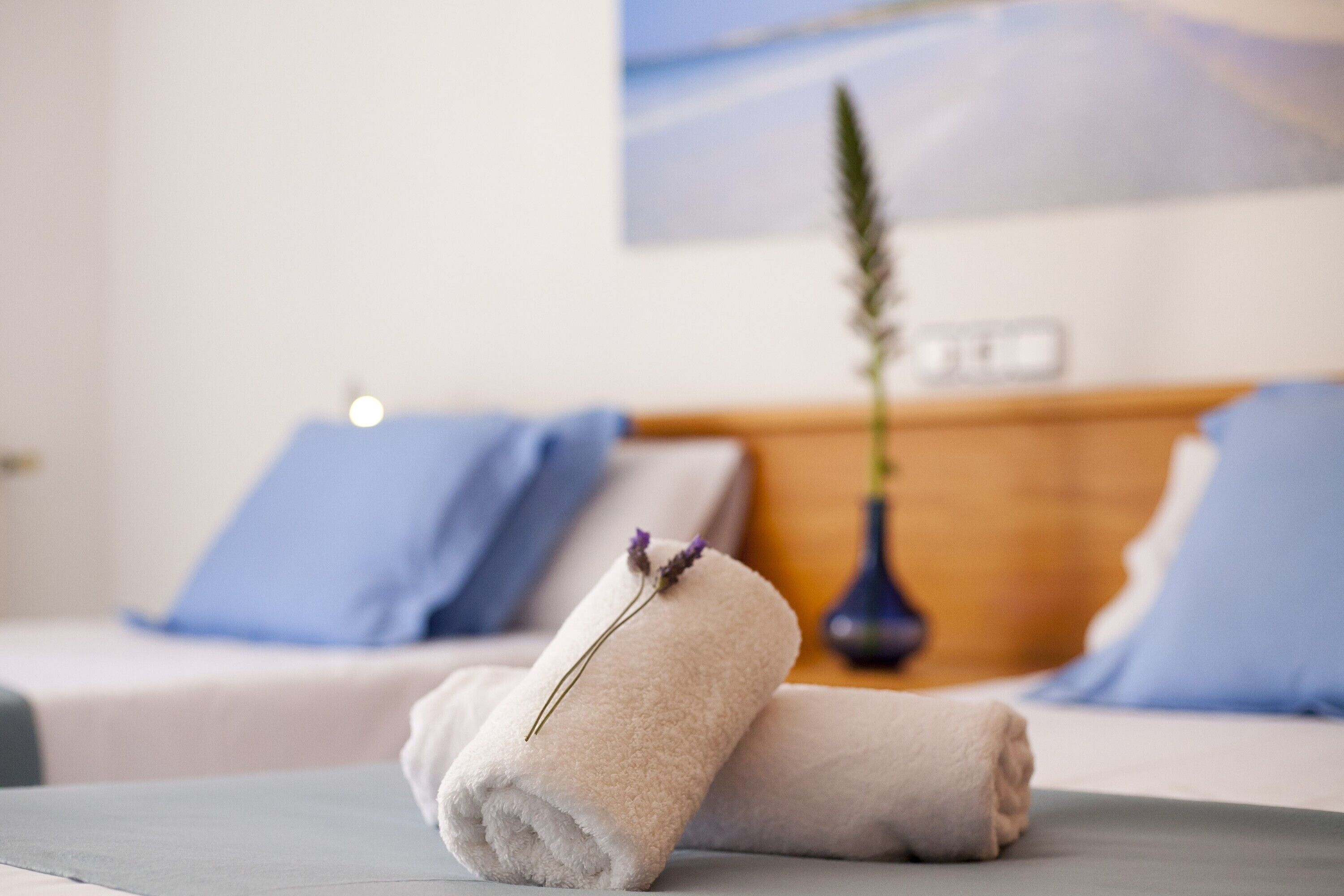 A neatly made bed with two pillows, a vase with a plant, and a sign on the wall.