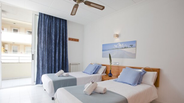 Een hotelkamer met twee bedden, uitzicht op buiten, een plafondventilator en een schilderij aan de muur.