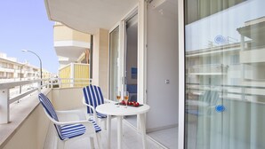 Een balkon met een witte tafel, twee gestreepte stoelen en een glazen deur.