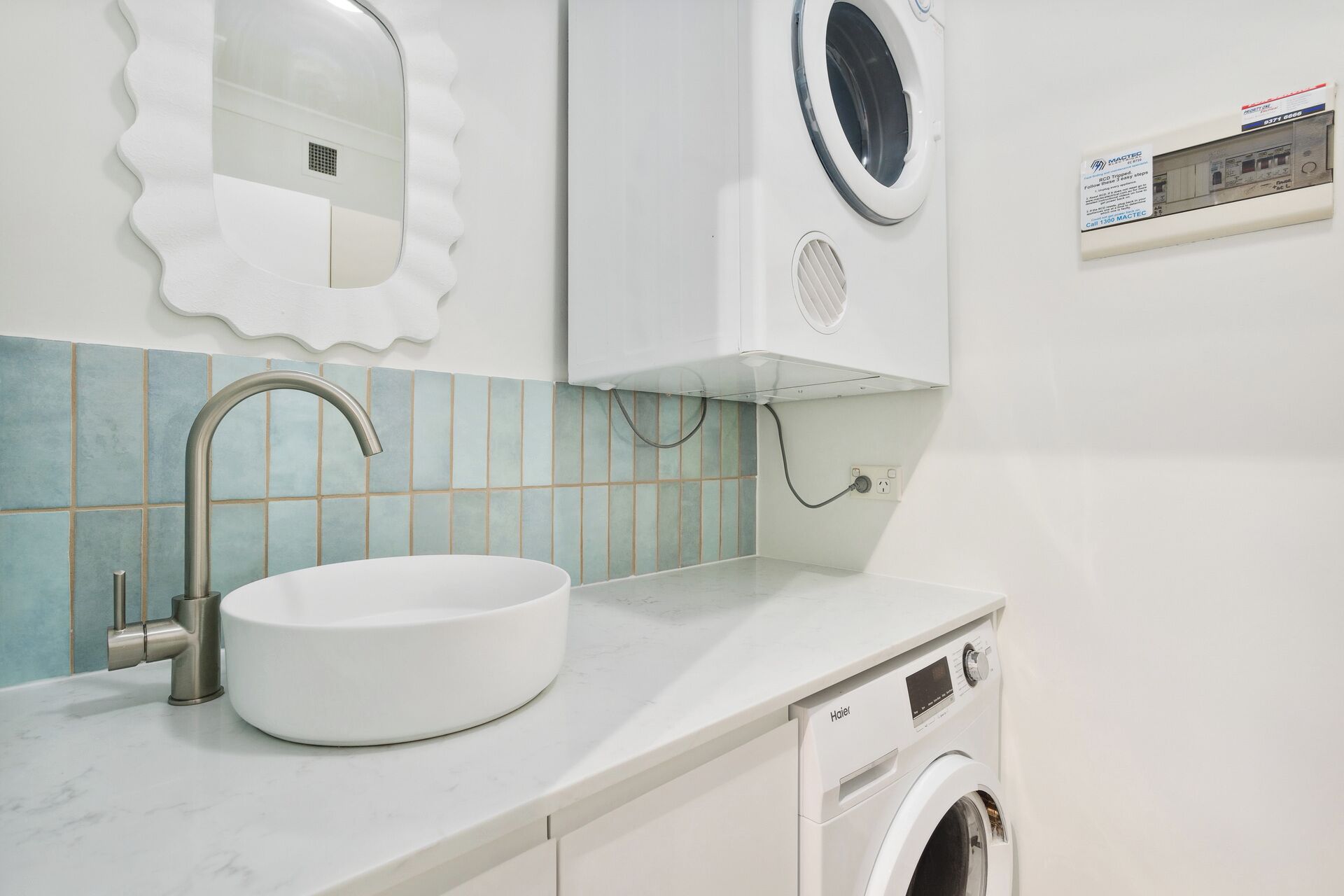 A bathroom with a sink, mirror, washing machine, and tiled backsplash.