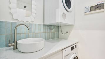 A bathroom with a sink, mirror, washing machine, and tiled backsplash.
