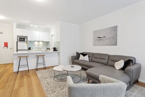 A modern apartment with a kitchen, a grey sofa, two bar stools, and a coffee table. - Modern & Relaxed, 2BR, Central with Courtyard & Parking (East Perth)