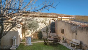 A courtyard with a stone wall, a tiled roof, a bench, and a table with chairs.