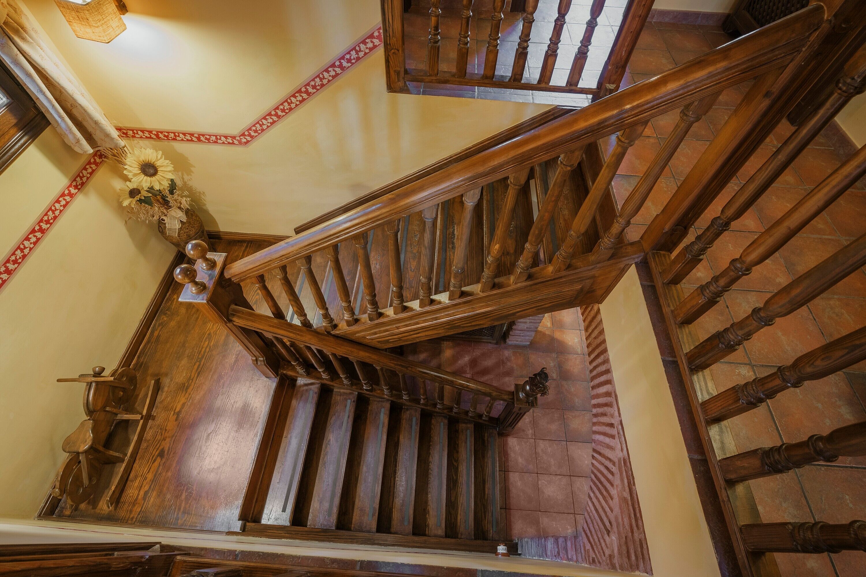 A wooden staircase with a handrail, a decorative vase with sunflowers, and a patterned border on the wall.