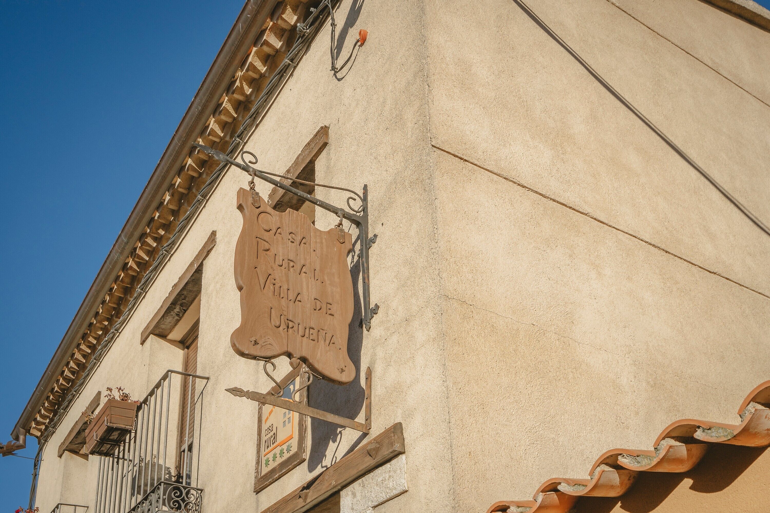 Un edificio con un letrero que dice 'Casa de Villa de Urueña' y un balcón con barandillas de metal.