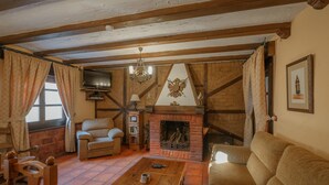 A rustic living room with exposed wooden beams, a fireplace, a television, and a sofa.