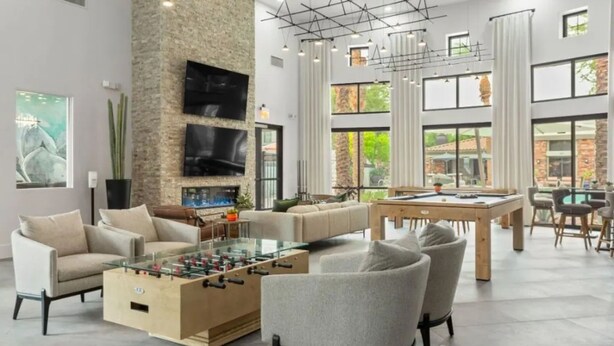 A modern living room with a foosball table, comfortable seating, a pool table, and large windows offering views of the outdoors. - Zone LUXE (Glendale)