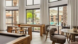 A poolside area with a pool table, seating, and large windows offering views of a pool and buildings. - Zone LUXE (Glendale)