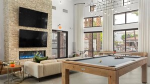 A pool table with a billiards cue, a sofa, and a television mounted on a stone wall. - Zone LUXE (Glendale)