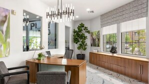 A modern office space with a wooden desk, two chairs, a large potted plant, and a view of the outside through large windows. - Zone LUXE (Glendale)