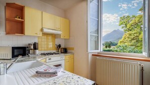A kitchen with yellow cabinets, a stove, a microwave, and a window with a mountain view. - Pyrénées Cottage with Mountain View, Private Terrace, and Wi-Fi – Top-Rated Accommodation (Lau-Balagnas)