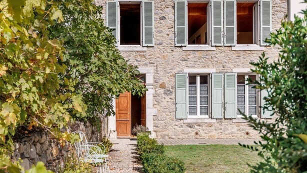 A stone building with a wooden door, multiple windows with shutters, and a paved path leading to the entrance. - Pyrénées Cottage with Mountain View, Private Terrace, and Wi-Fi – Top-Rated Accommodation (Lau-Balagnas)