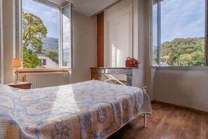 A bedroom with a bed, a nightstand, a lamp, a fireplace, and a view of the outdoors.
