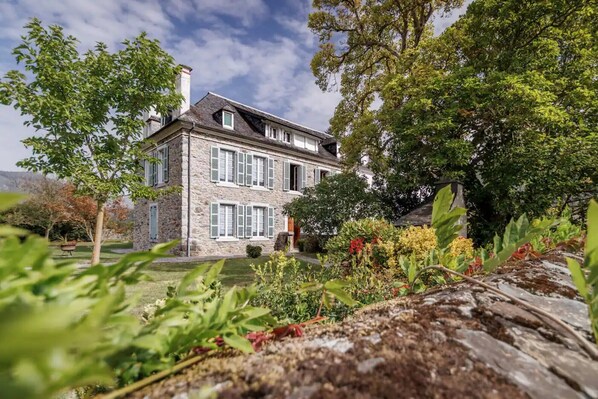 A stone building with multiple windows and a garden in the foreground.