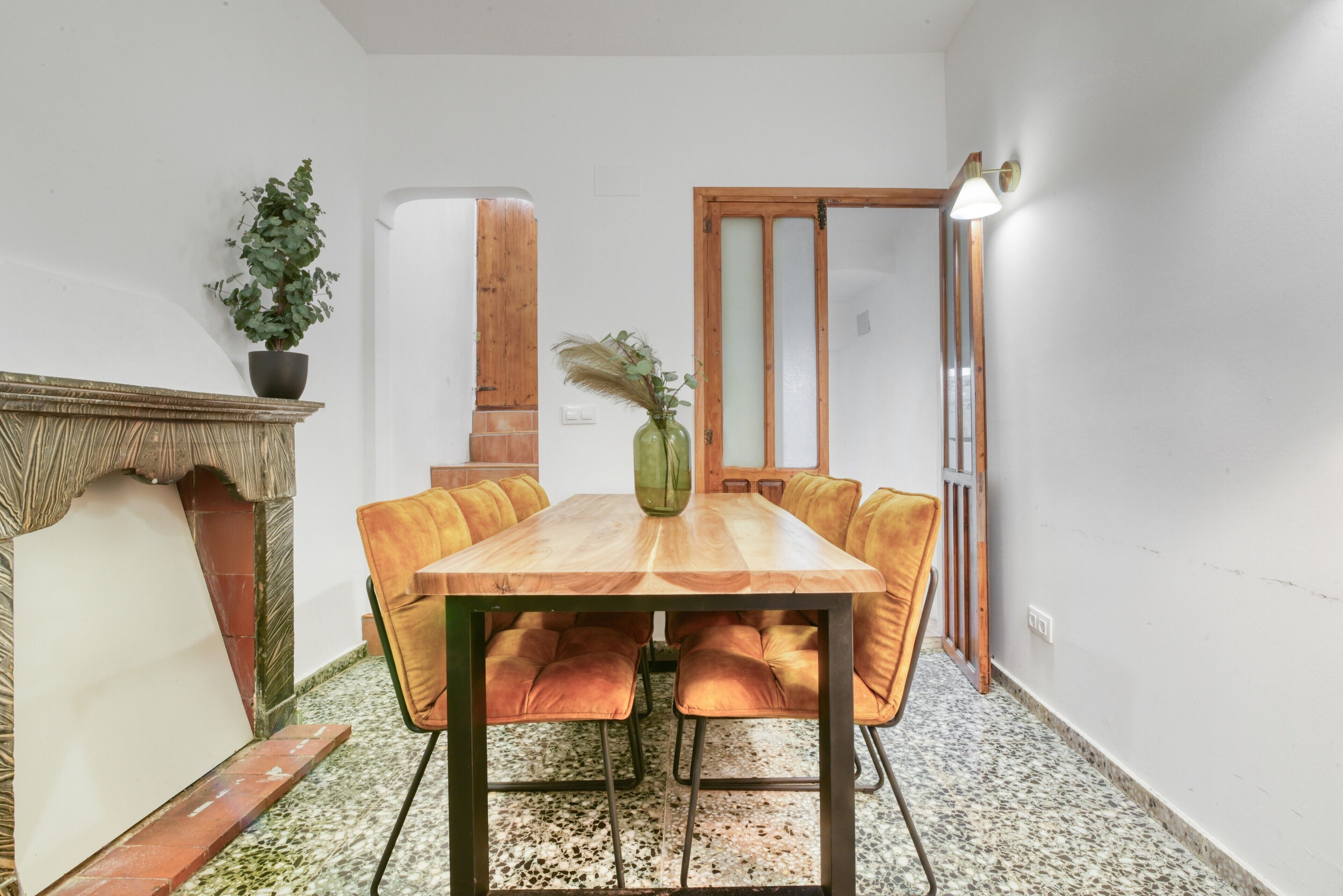 A dining area with a wooden table and cushioned chairs, a fireplace, and a potted plant.