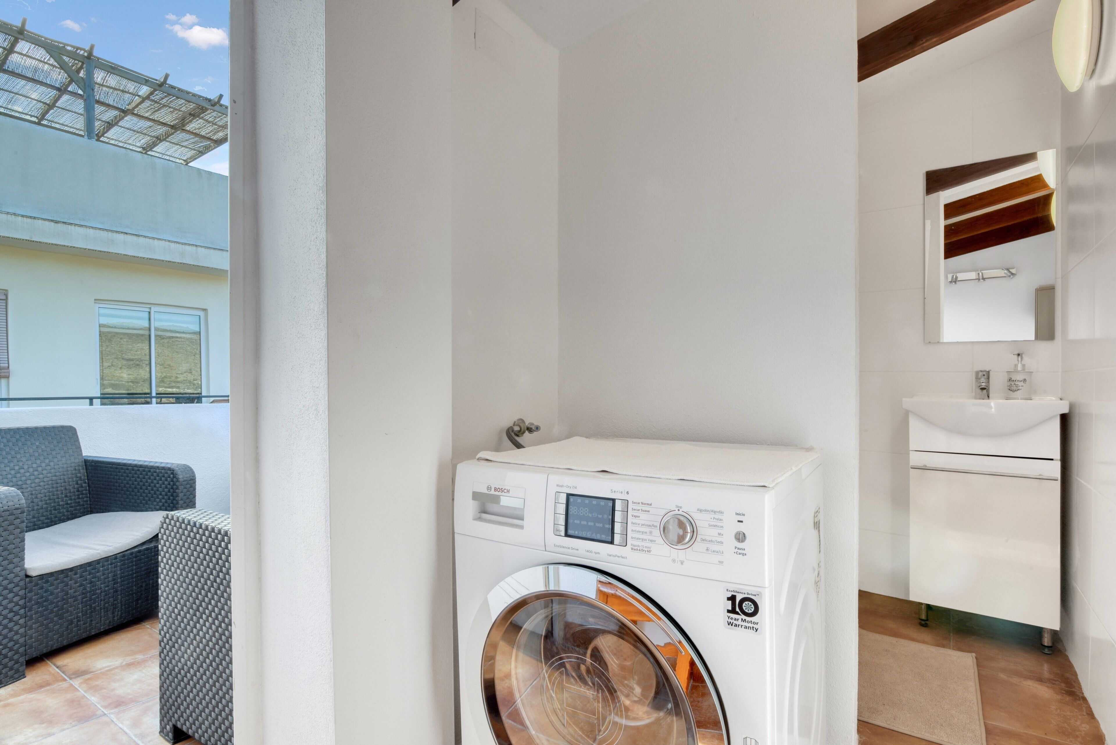 A compact room with a washing machine, a small sink, and a balcony with outdoor seating.