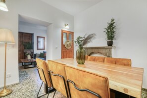 Een eetruimte met een houten tafel, lederen stoelen, een vaas met gedroogde planten en een potplant aan de muur.