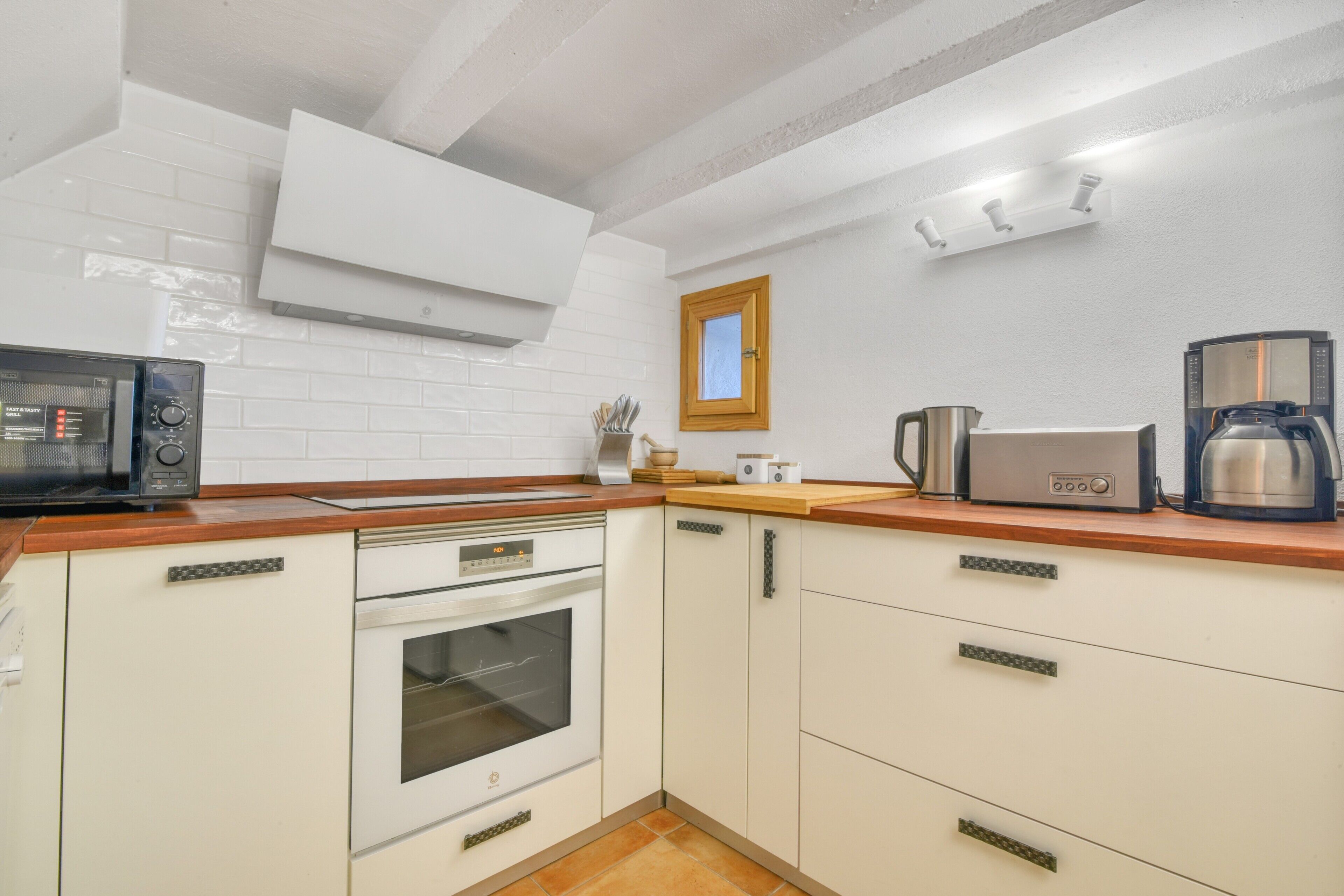 A kitchen with white cabinets, a microwave, a coffee maker, and a window.
