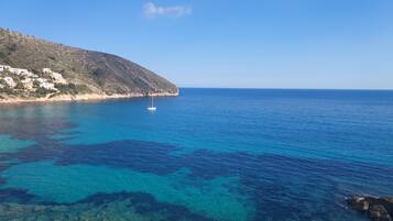 Un paysage côtier avec une eau bleue et limpide, un bateau et une colline parsemée de bâtiments.