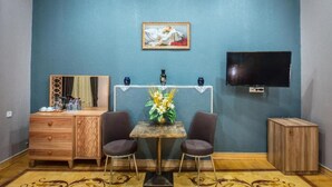 Una habitación con un aparador de madera, dos sillas, una mesita con un florero, un cuadro en la pared, un televisor y un aire acondicionado.