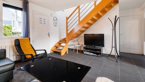 Una sala de estar moderna con una mesa de centro de vidrio negro, una escalera de madera, un televisor y un sofá.