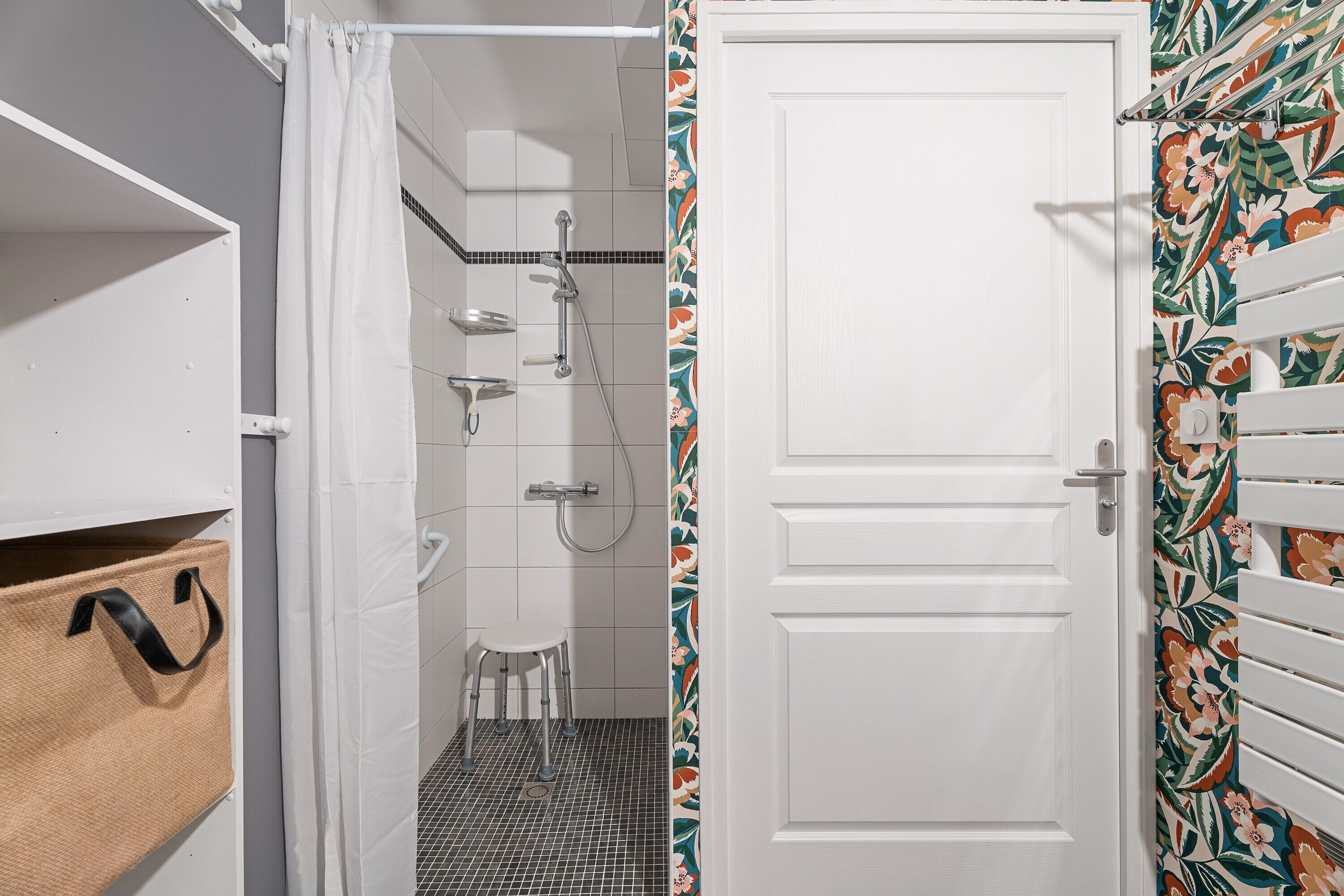 Un bagno con doccia, toilette e lavabo. Una porta bianca con carta da parati a motivi floreali.