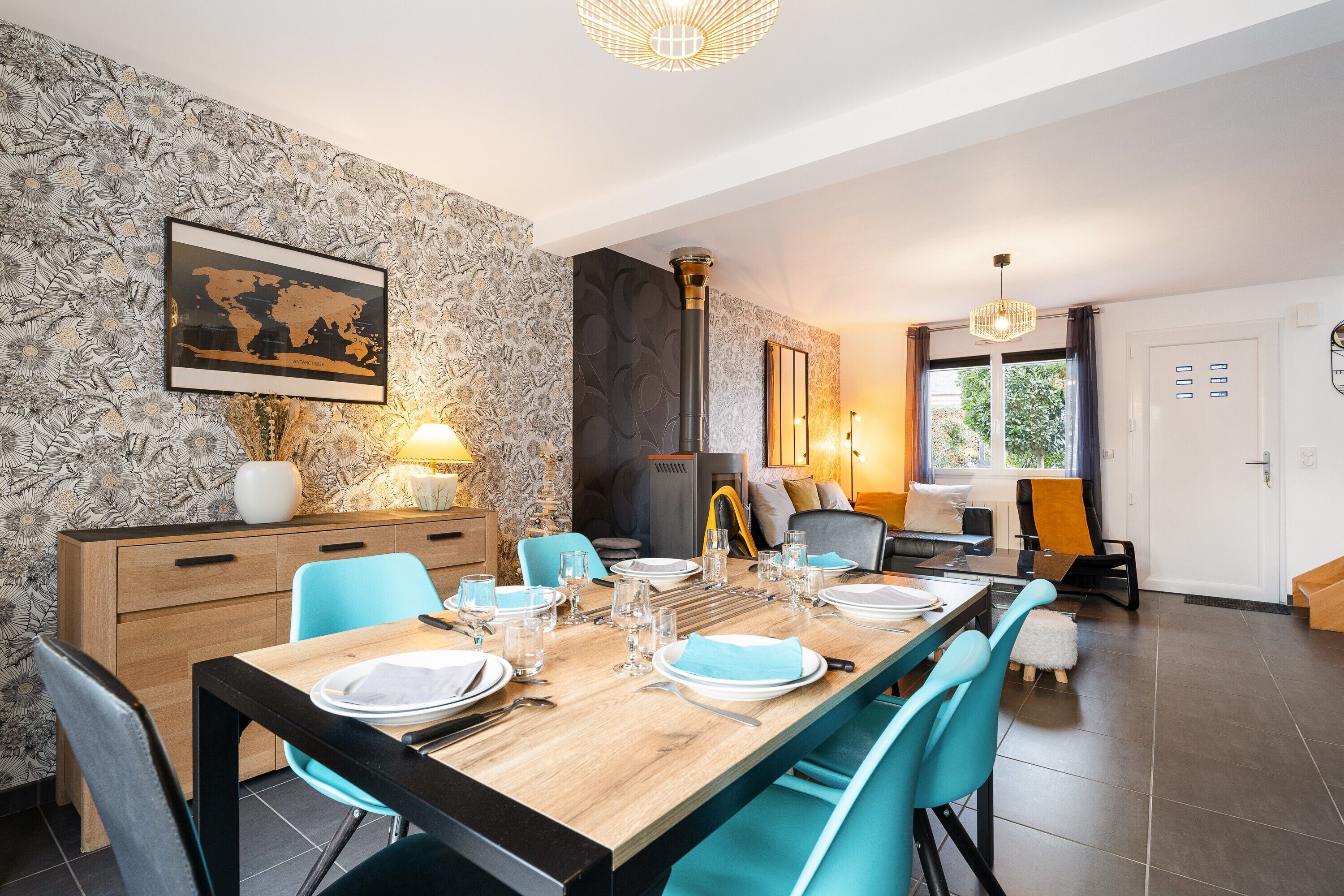 A dining area with a wooden table set for four, blue chairs, a world map on the wall, and a fireplace.