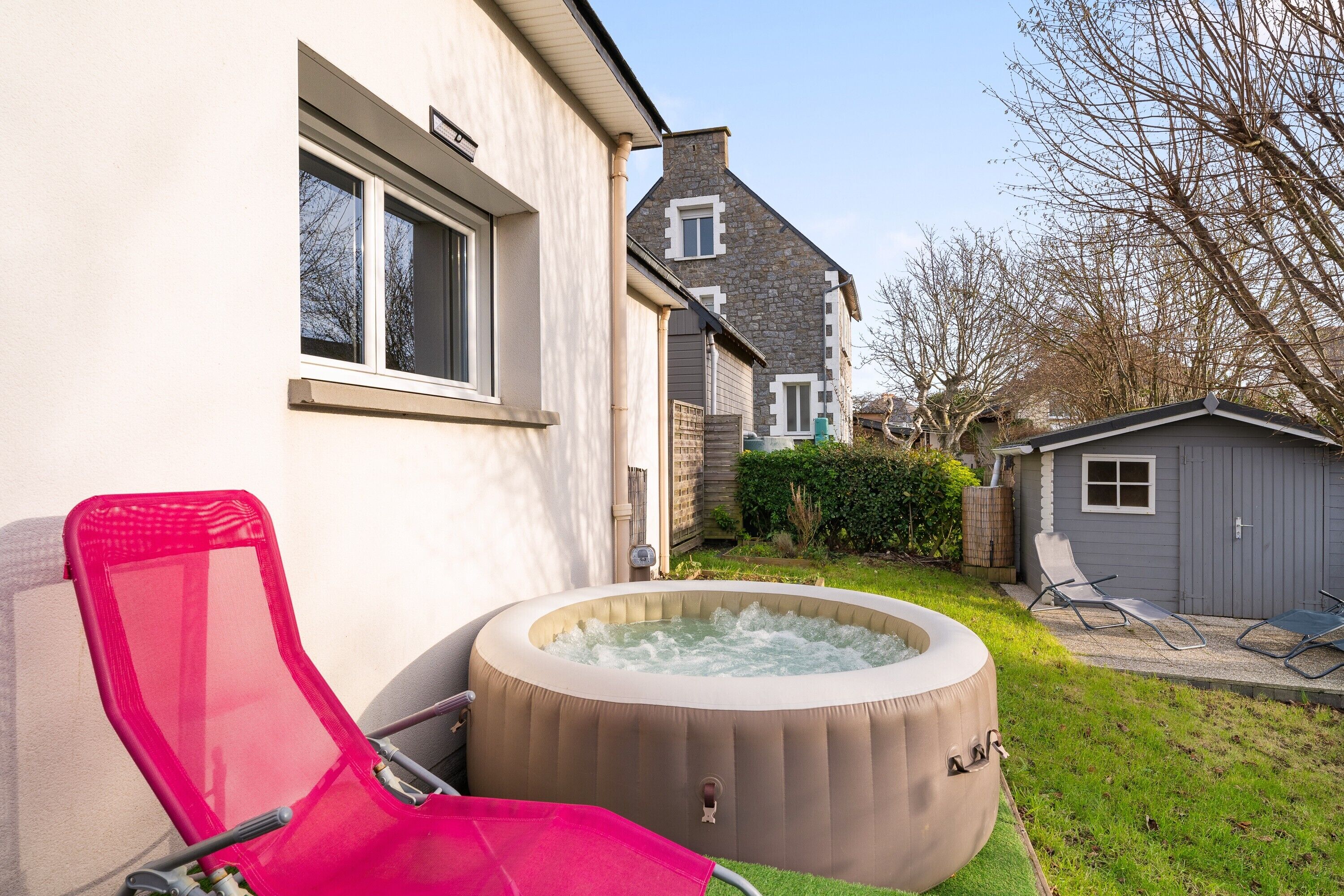 A backyard with a hot tub, a red lounge chair, and a small shed.