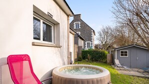 Un patio trasero con un jacuzzi, una silla de descanso roja y un cobertizo pequeño.