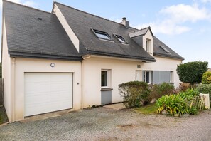 Une maison à deux étages avec un garage, deux fenêtres de toit et un petit jardin.
