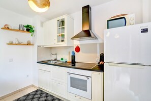 Moderni keittiö, jossa on valkoiset kaapit, ruostumattomasta teräksestä valmistettu liesituuletin, sisäänrakennettu mikroaaltouuni ja jääkaappi.