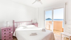 Quarto com cama, mesa de cabeceira, cômoda e varanda com vista.