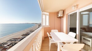 Varanda com vista para a praia, uma mesa com cadeiras e uma porta de vidro deslizante.