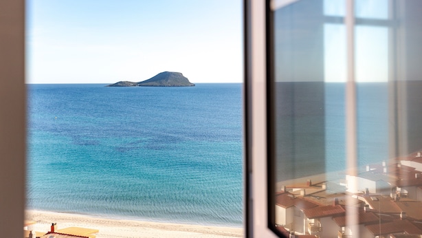 Vista costeira através de uma janela, mostrando uma praia, mar calmo e uma ilha distante.