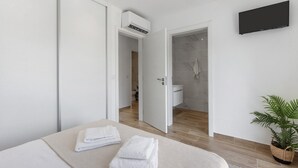 A modern hotel room with a bed, a flat-screen TV, an air conditioning unit, a potted plant, and a bathroom visible through an open door. - Holiday Home 'Refugio Das Vinhas' with Mountain View, Wi-Fi and Air Conditioning (Celorico de Basto)
