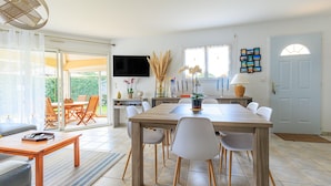 A dining area with a wooden table and chairs, a TV mounted on the wall, and a view of the outdoors through a glass door.
