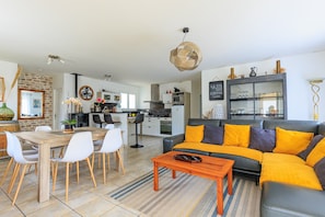 A modern living room with a sectional sofa, dining table, and chairs. There is a kitchen in the background with cabinets and appliances. - Villa Melchivany – Nature & Ocean, Terrace, Garden, Spa for 6 People in Messanges (Messanges)